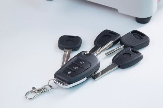 Car keys, including a remote key fob, scattered on a white surface.