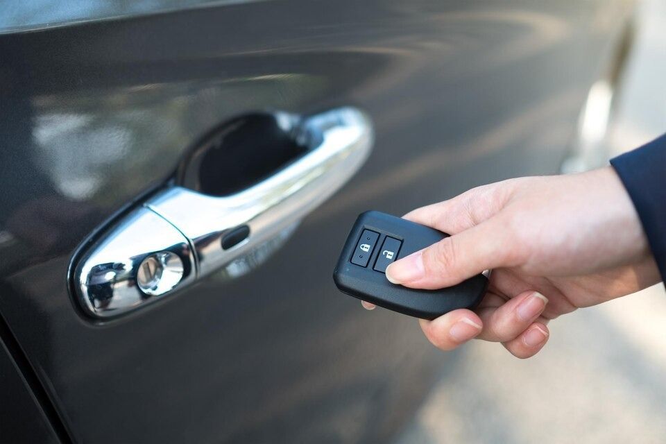 Hand holding a car key remote, unlocking a dark grey car door.