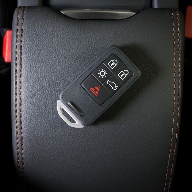 Car key on a black leather car seat, with orange stitching and an emergency light button.
