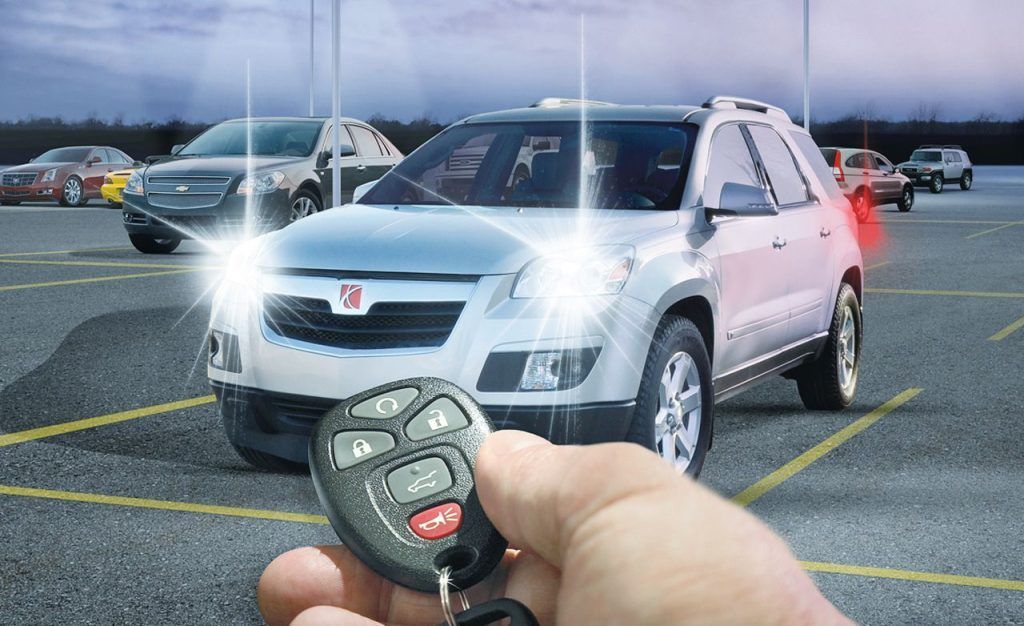 Person unlocking a white SUV in a parking lot with a key fob, headlights on.