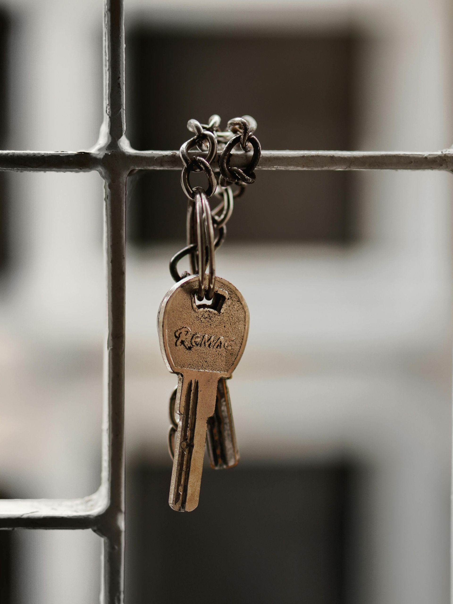 Keys hanging from a metal gate, silver chain, blurred background.