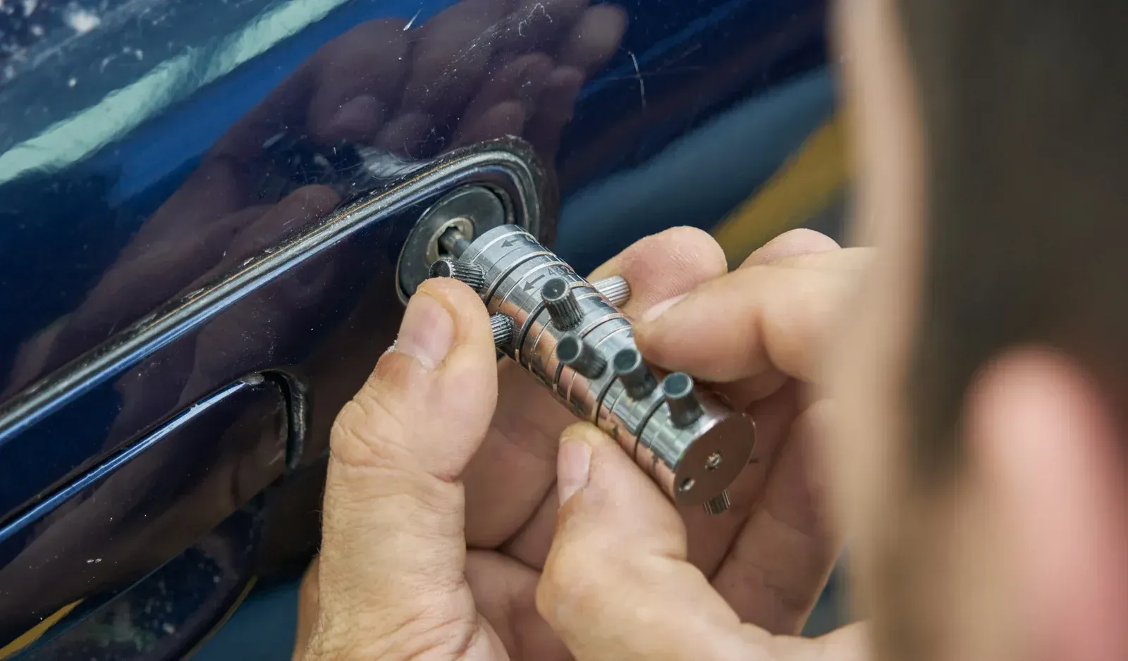 Person installing a car door lock, hands holding the cylindrical mechanism against the blue car door.
