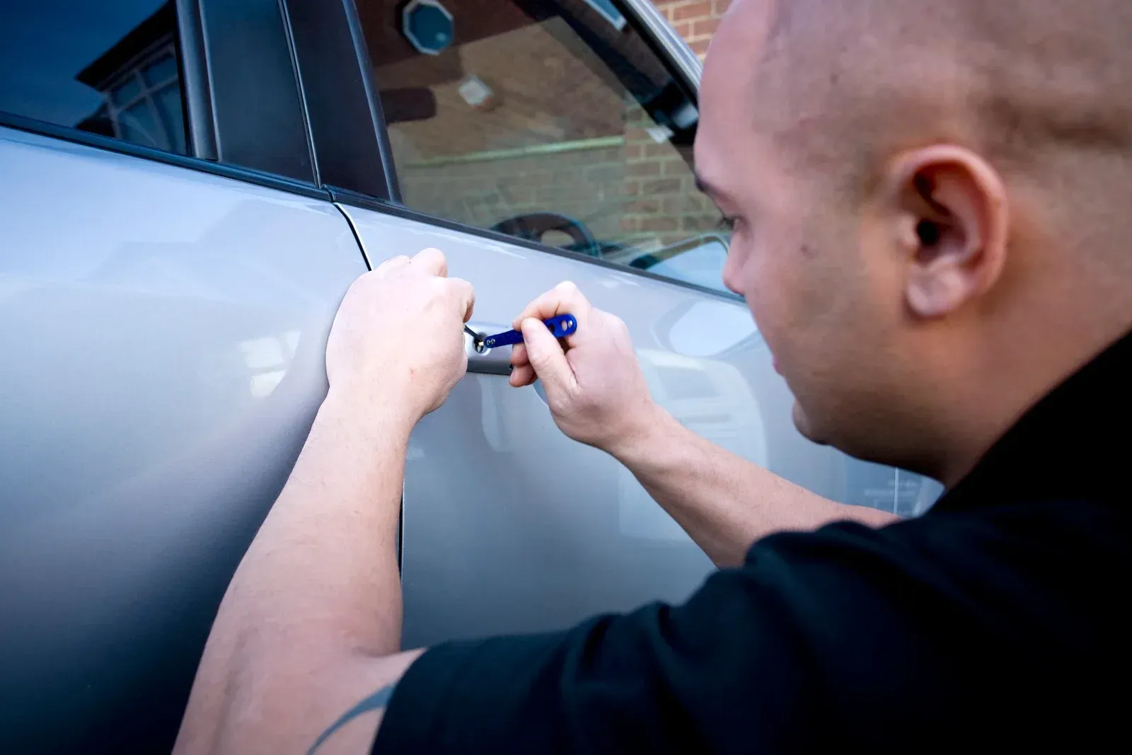 Man using a tool to try and open a car door.