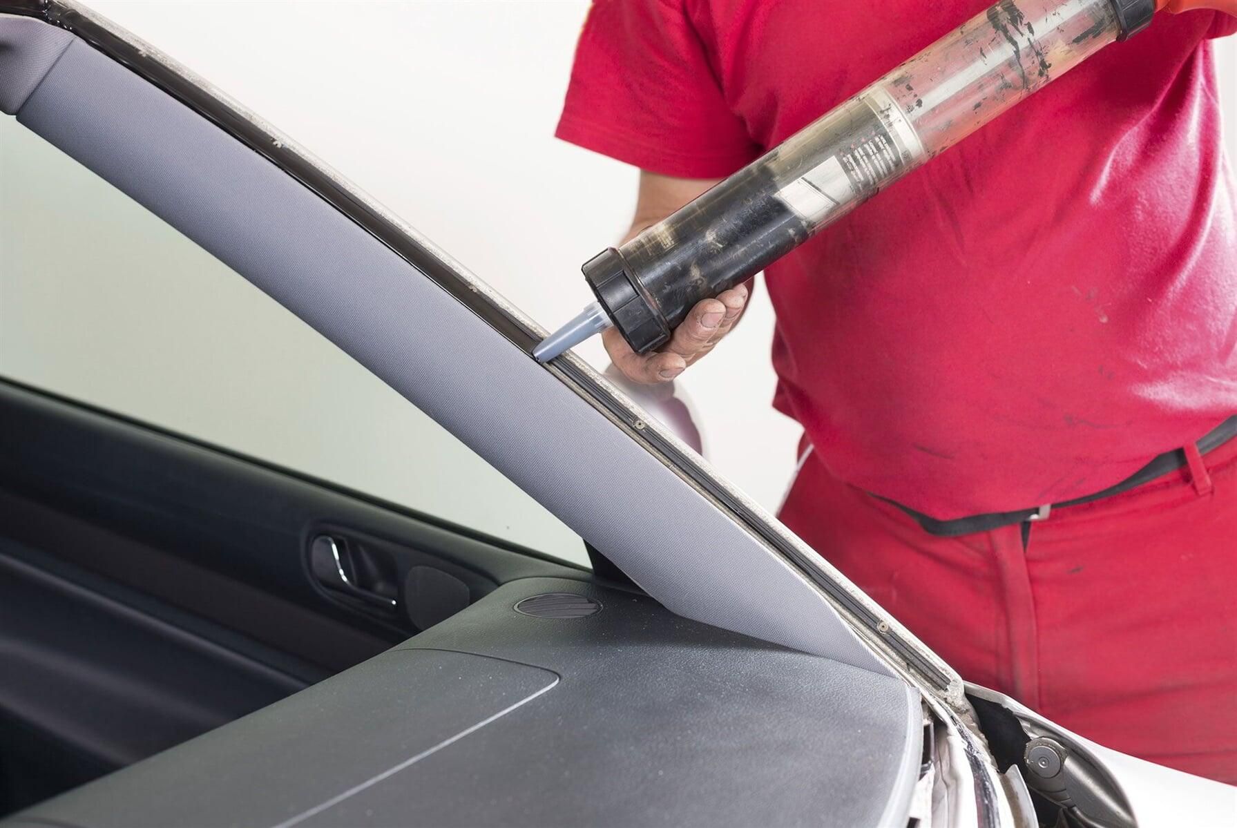 Un hombre con una camisa roja está instalando un parabrisas en un automóvil.
