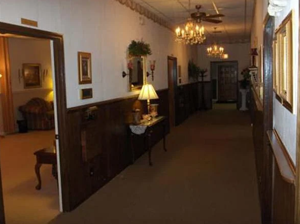 Long hallway in a building with wood paneling, ornate lights, and doors leading to rooms.