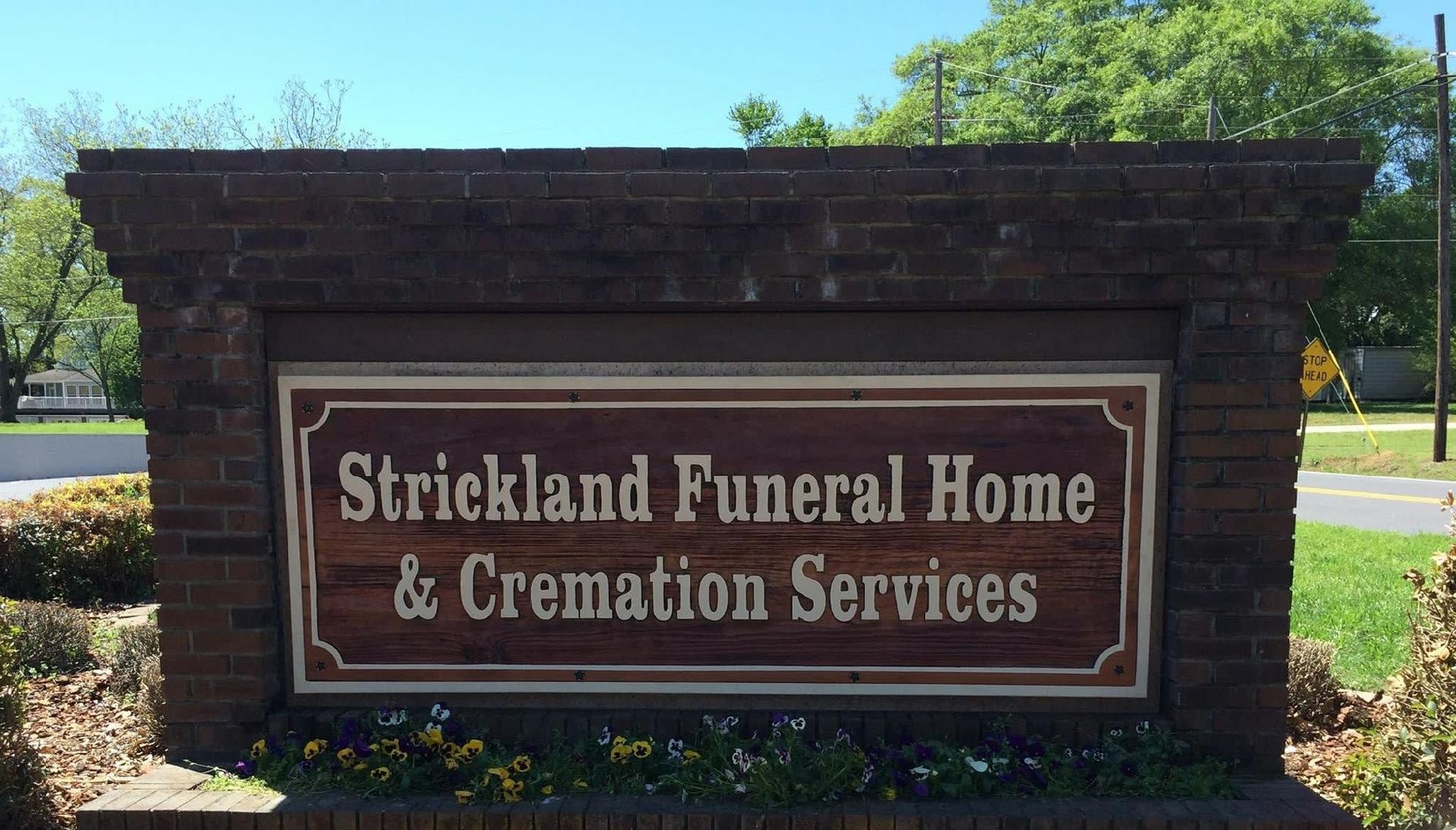 Strickland Funeral Home & Cremation Services sign, brown lettering on wooden background, brick border.