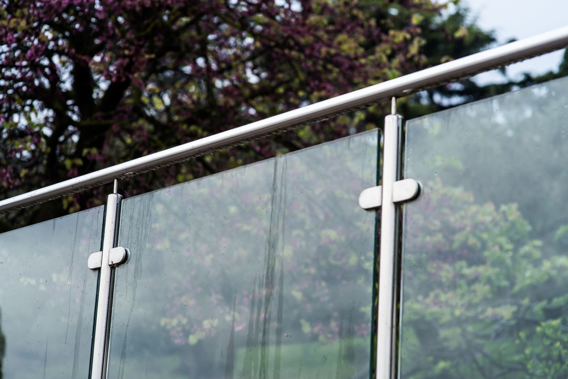 Un gros plan d'une balustrade en verre avec des arbres en arrière-plan.