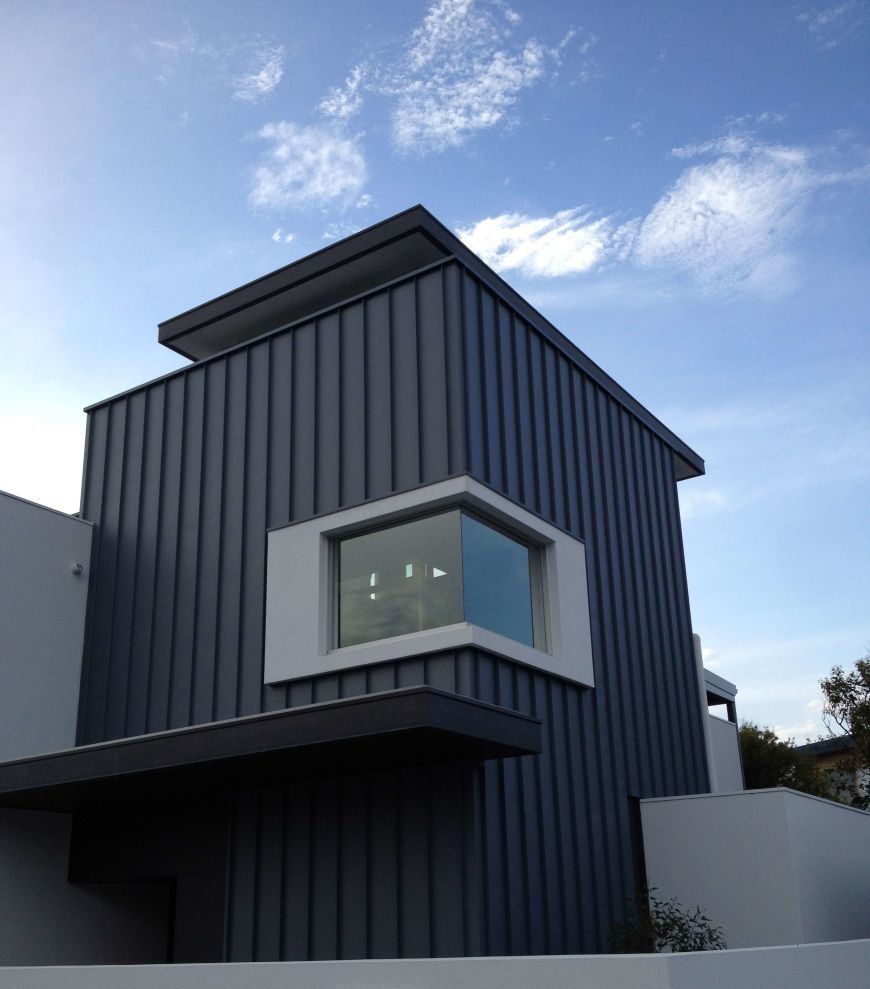 Modern building with gray vertical siding, white window frame, and a blue sky.