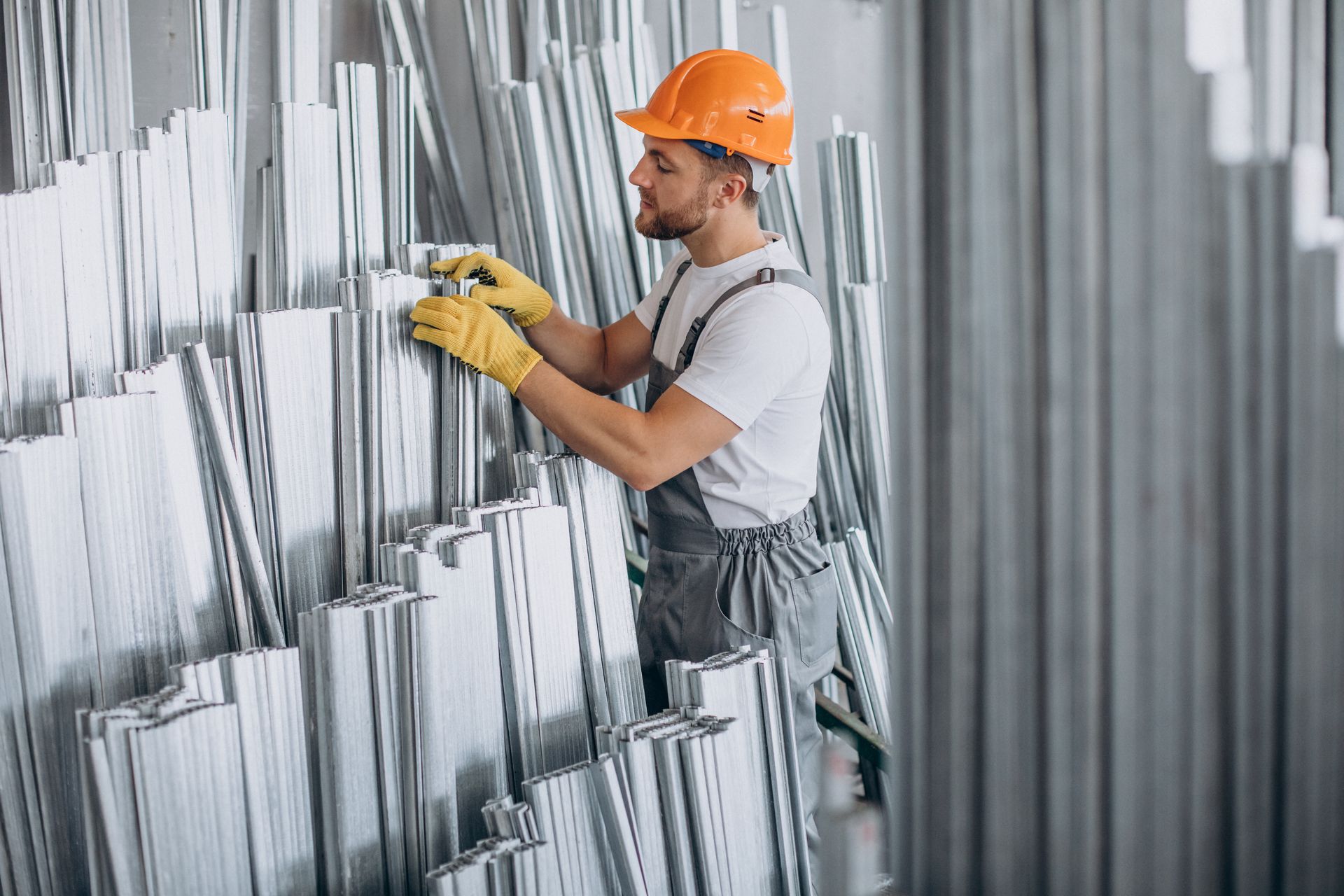 A man wearing a hard hat and yellow gloves is working on a wall.