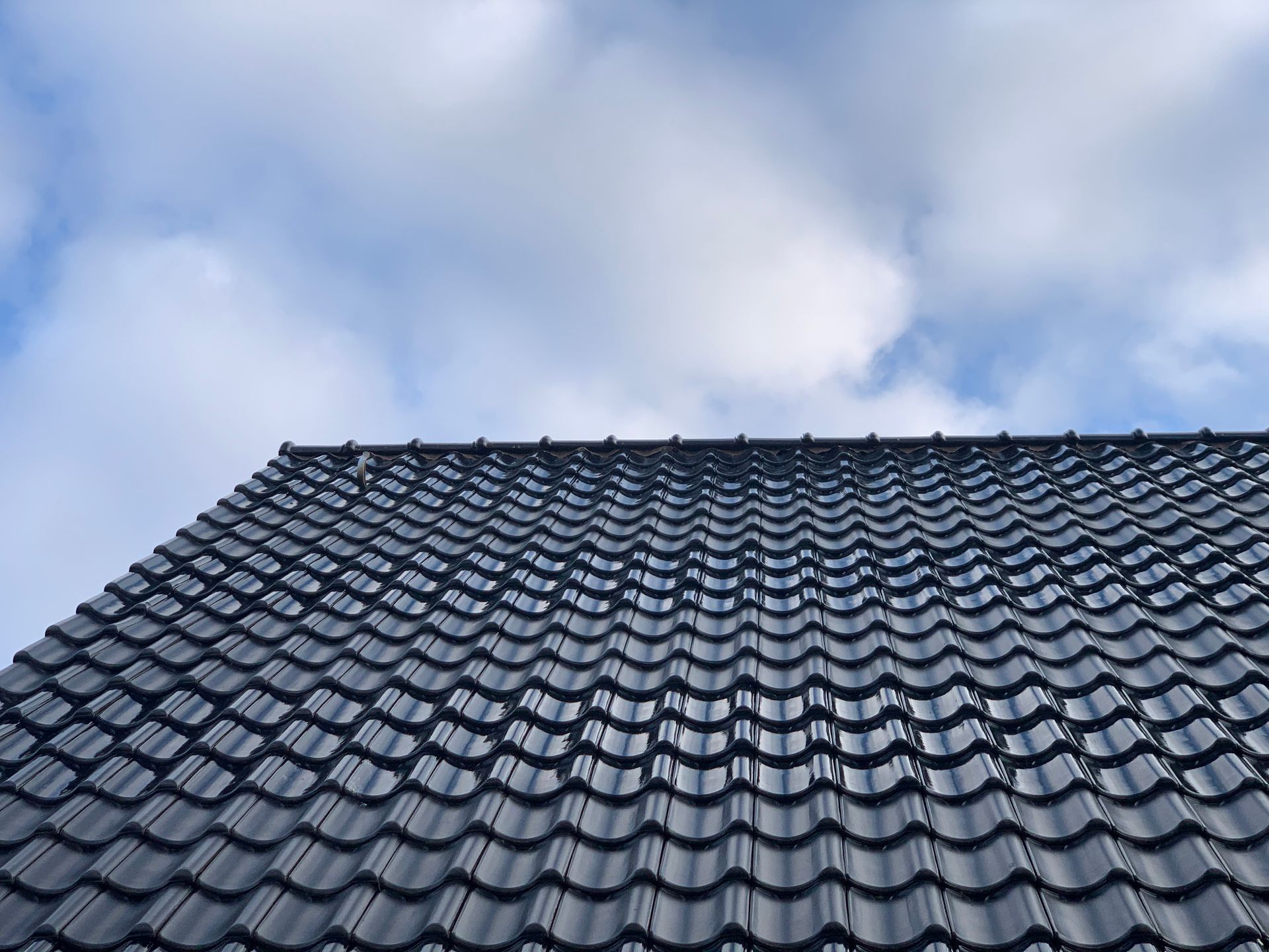 Looking up at a black tiled roof with a blue sky in the background.