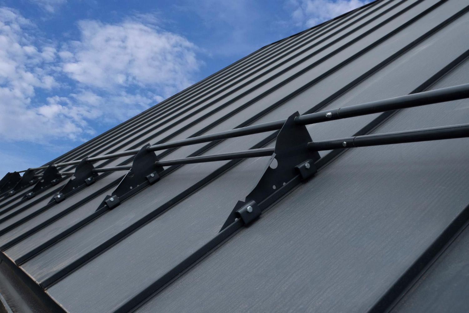 Dark gray metal roof with horizontal bars and supports against a partly cloudy blue sky.