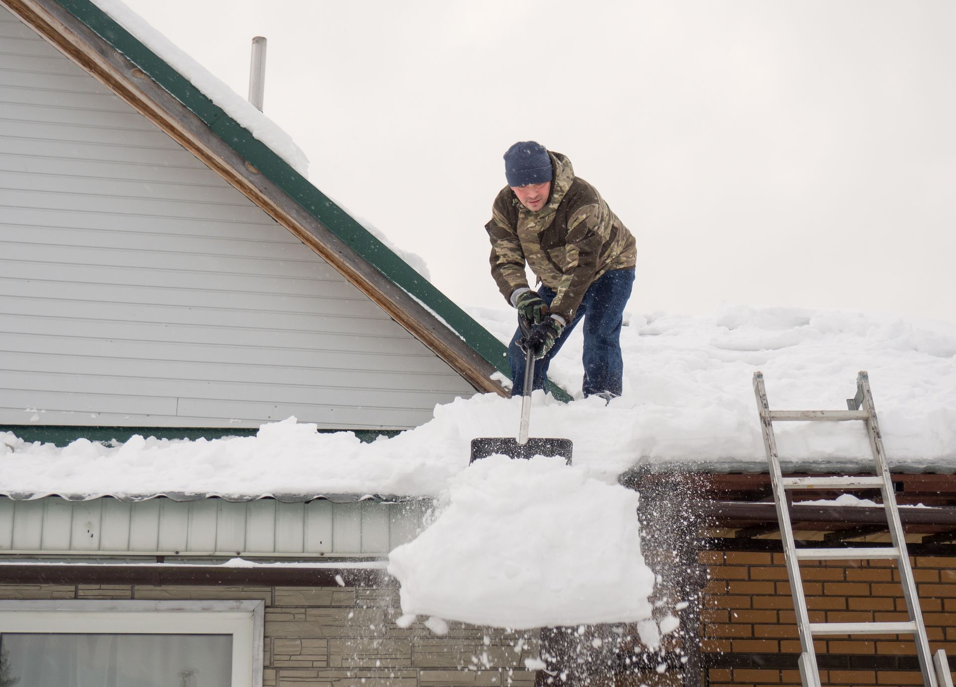 A man is shoveling snow from the roof of a house.
