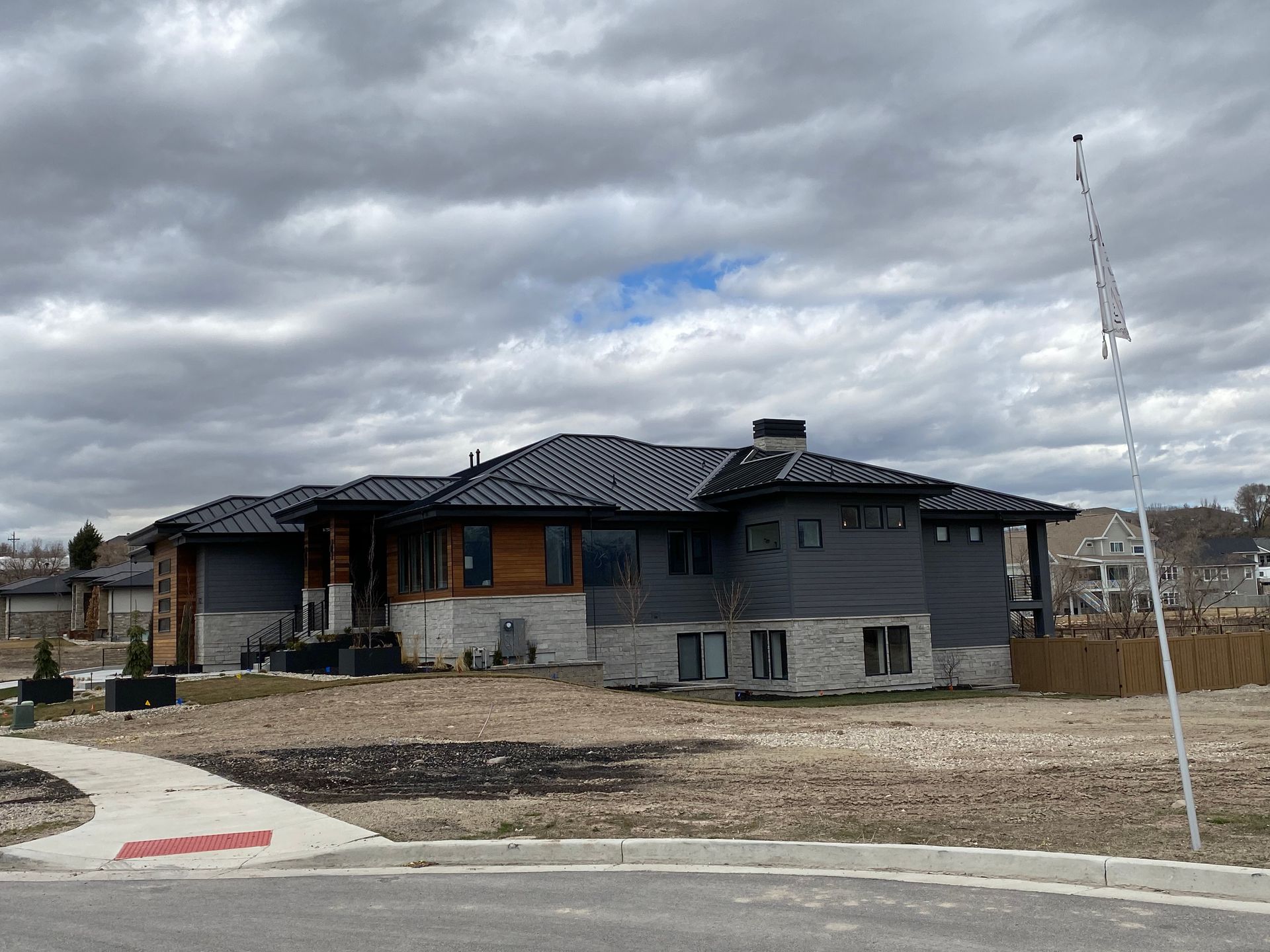 Modern home under a cloudy sky, with gray siding, wood accents, and a dark tiled roof.
