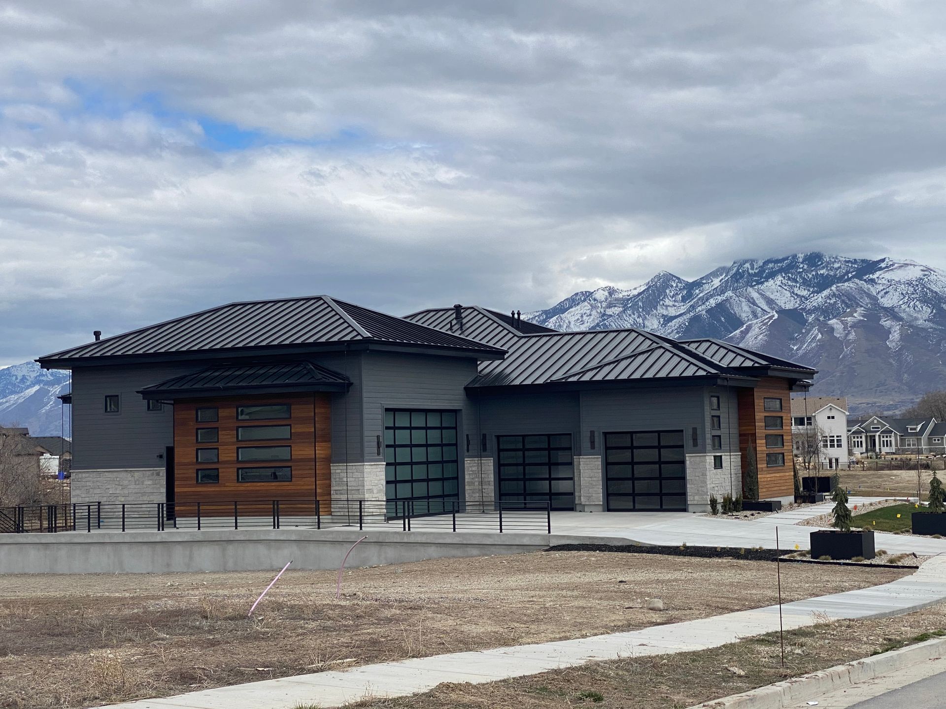 Modern gray house with glass garage doors, wood accents, and a mountain backdrop.