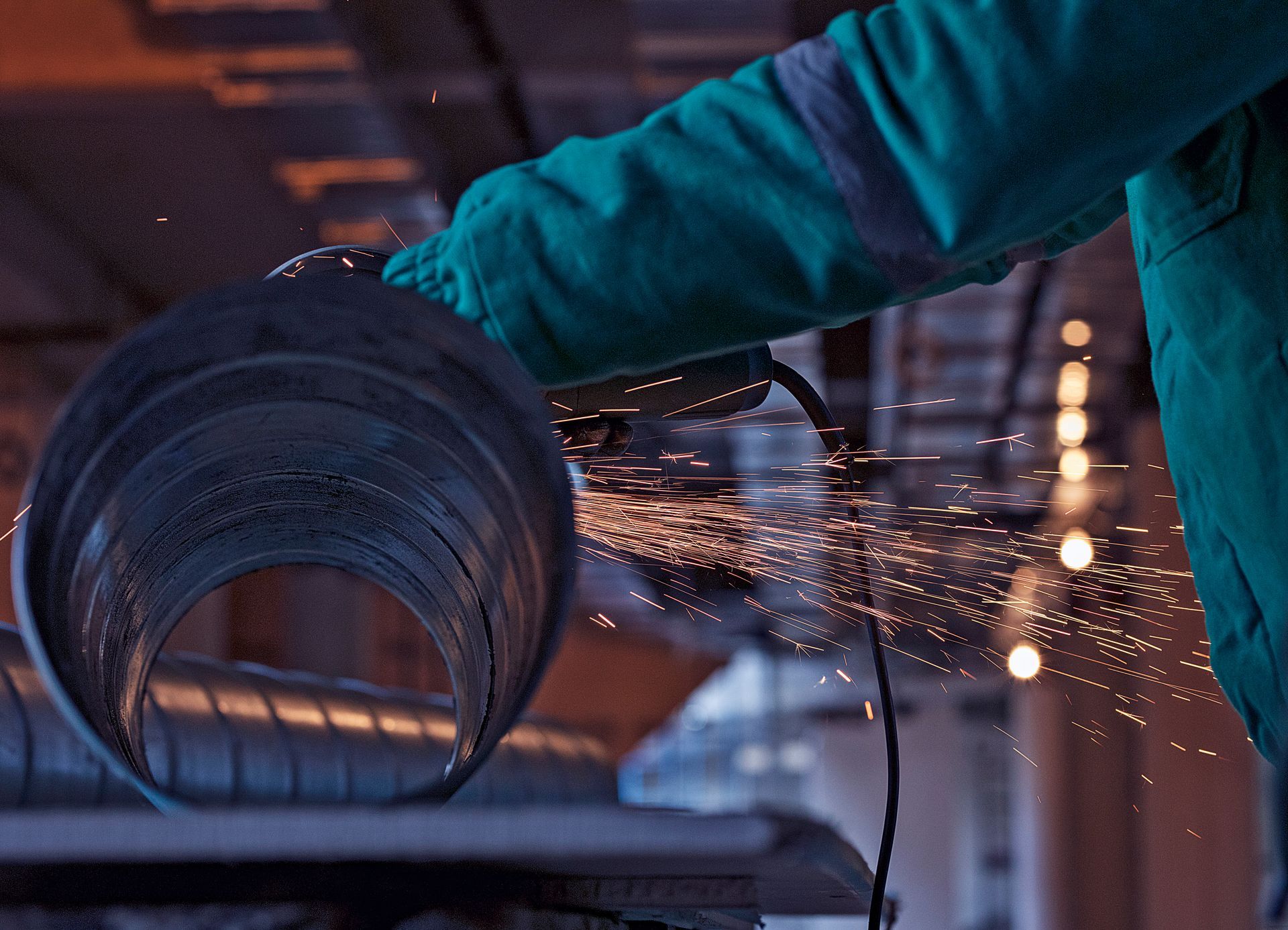 A person is cutting a metal pipe with a grinder.