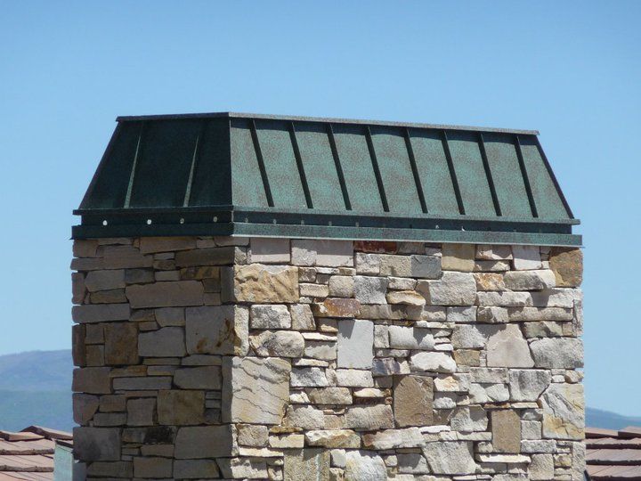 A stone chimney with a green roof on top of it