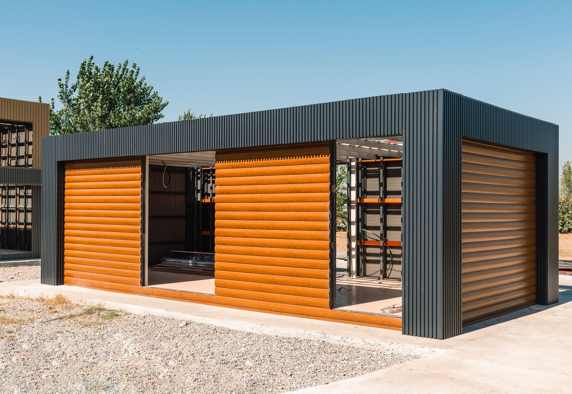 Modern outdoor structure with sliding wooden doors, surrounded by gravel, against a clear blue sky.