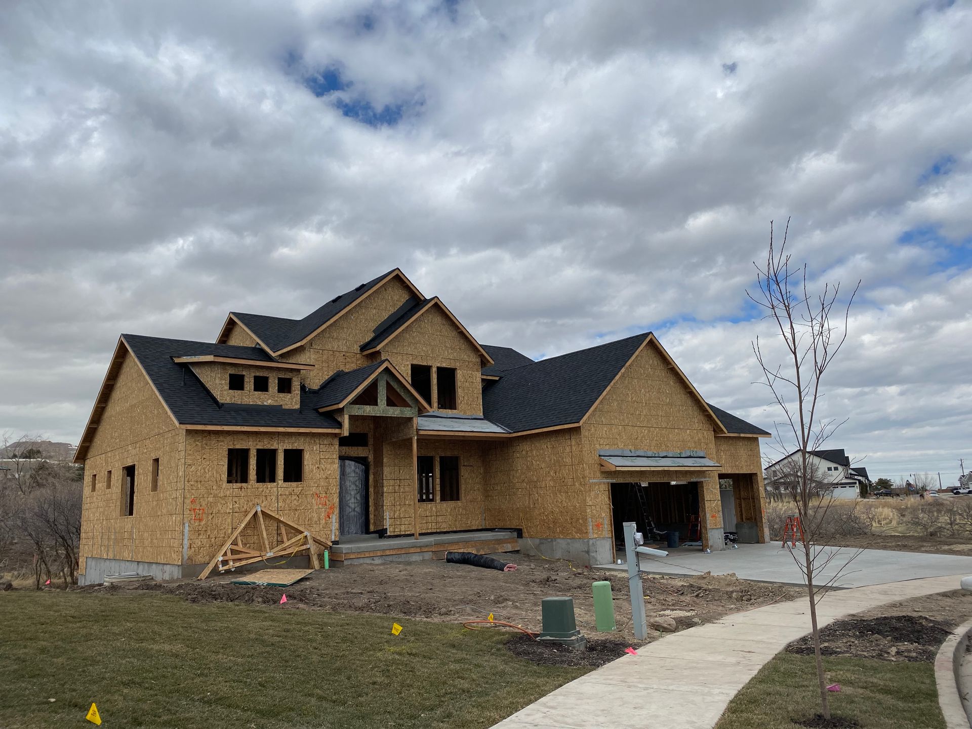 New house under construction with exposed wood, gray roof, and a cloudy sky.