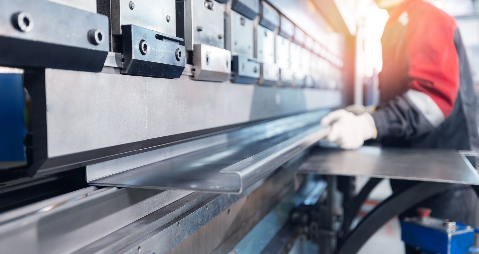 Person bending metal sheet with a press brake machine in a workshop.