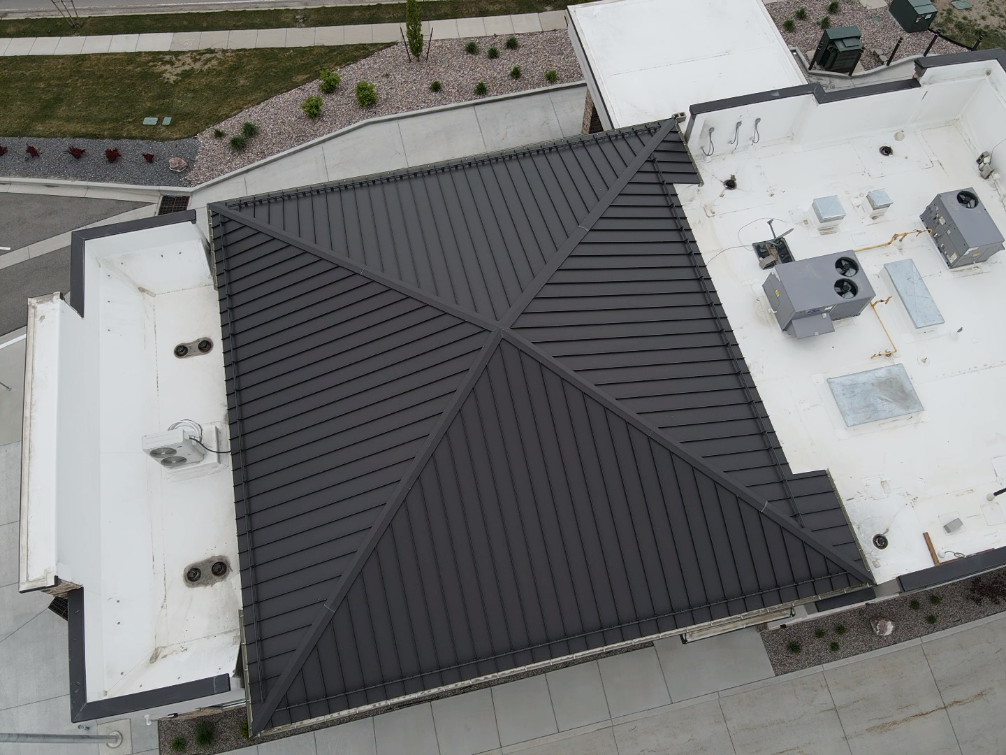 Overhead view of a building with a dark gray metal roof and white flat roof sections.