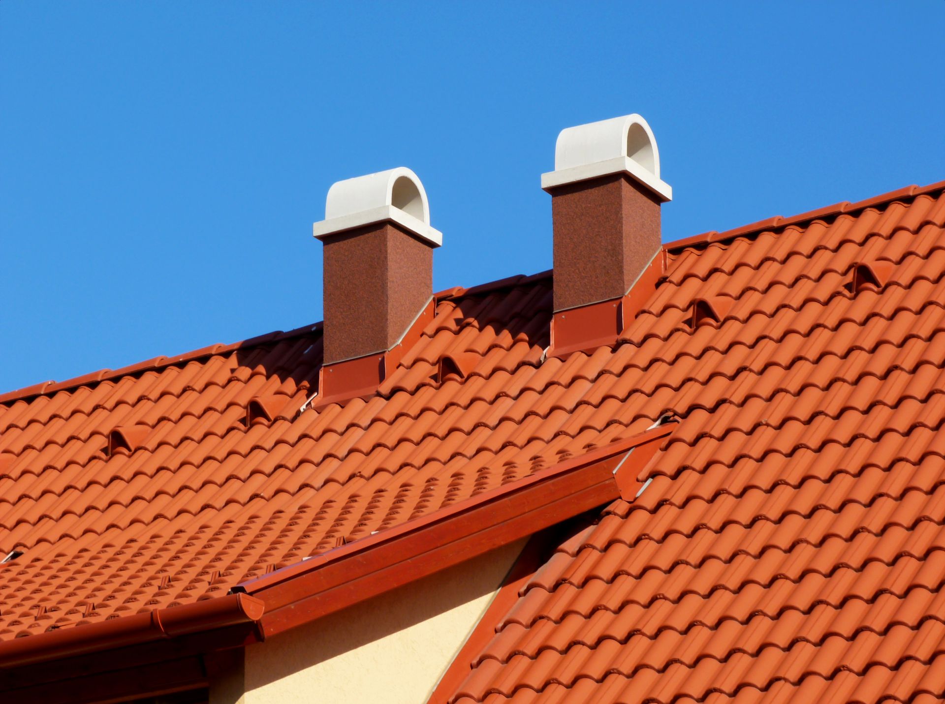 Two chimneys on top of a red tiled roof