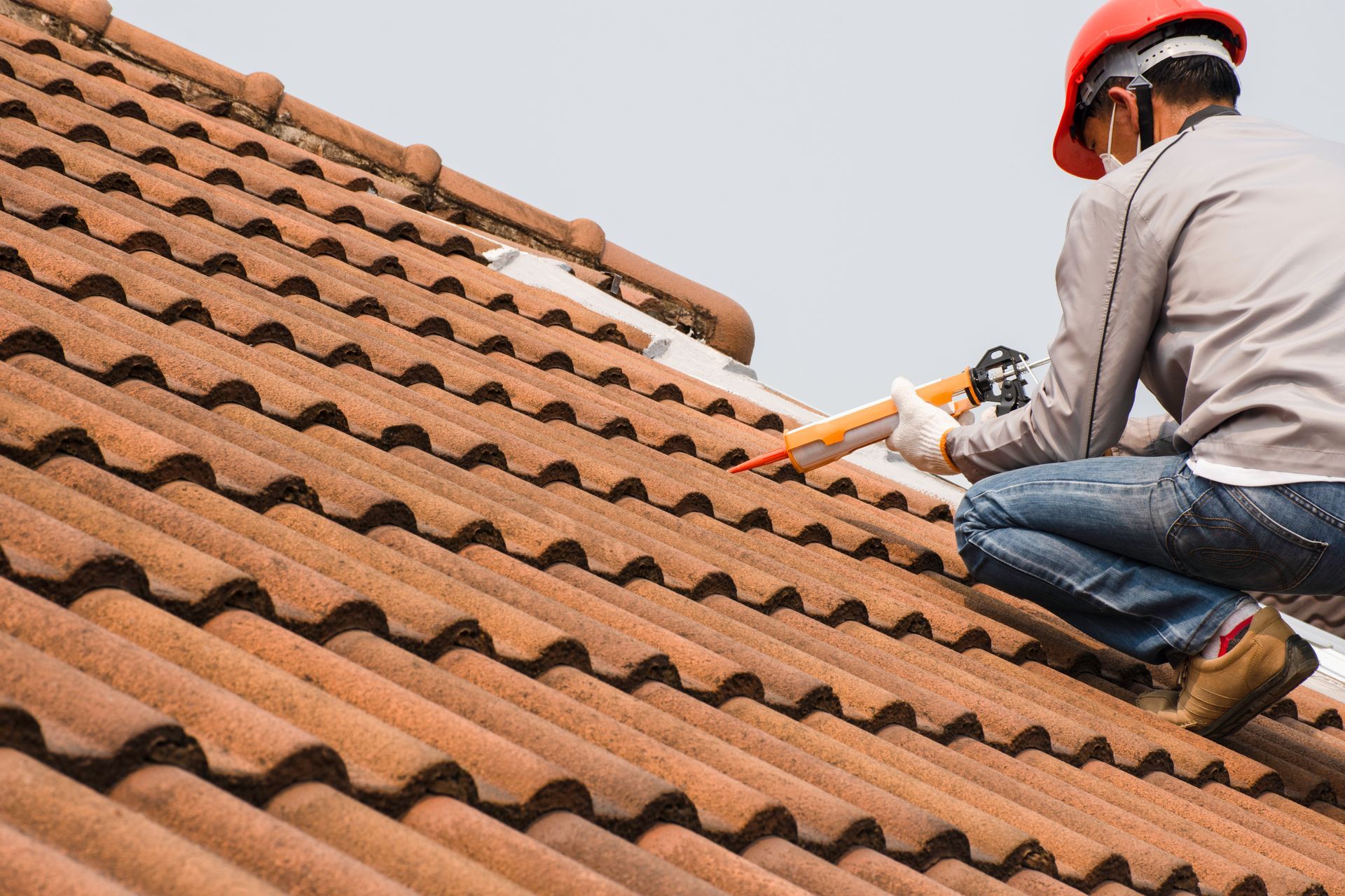 A man is kneeling on top of a tiled roof.