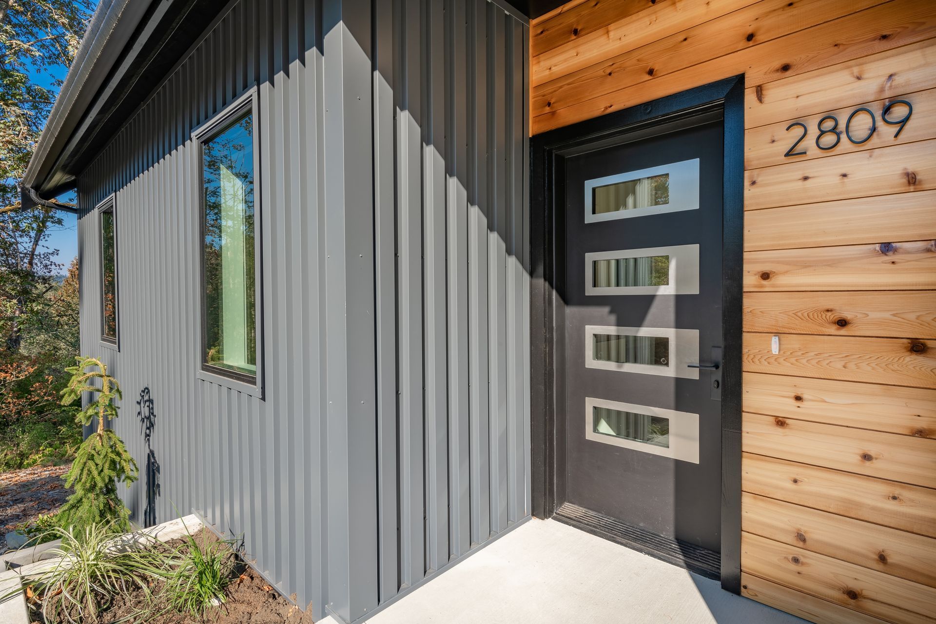 A modern house with a gray siding and a black door.