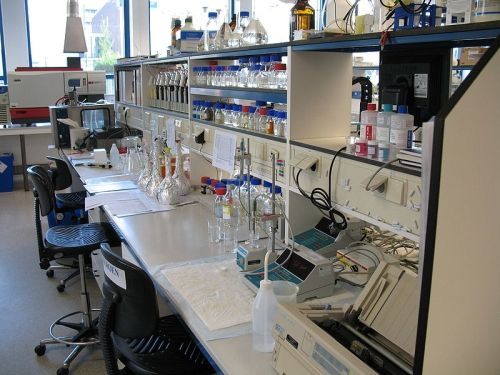 Laboratoriumtafel met glaswerk, apparatuur en krukjes in een licht onderzoekslaboratorium.