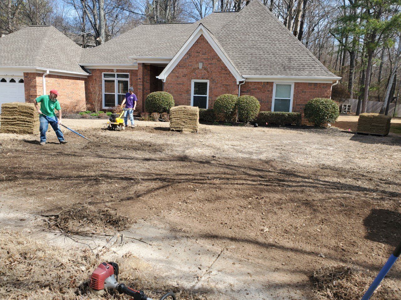 People preparing lawn for sodding, brown soil, house in background.