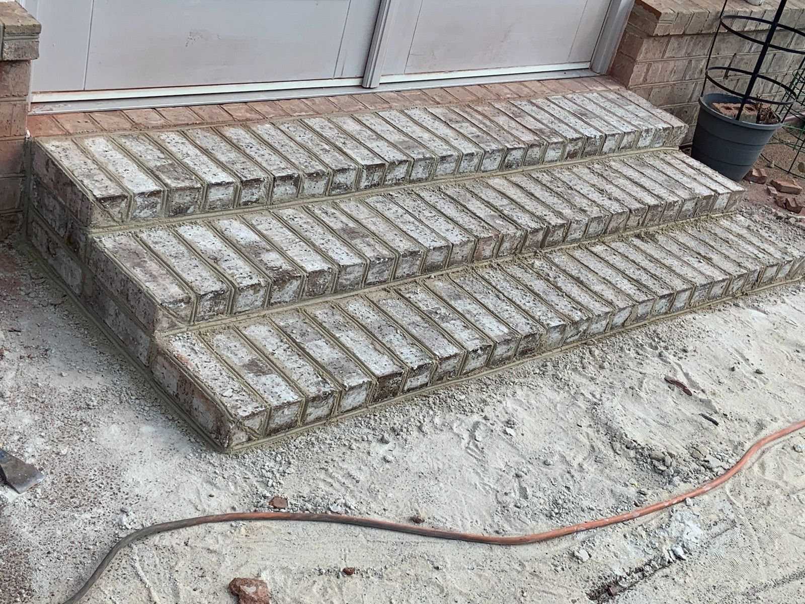 A hose is laying on the ground next to a set of brick steps.