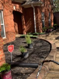 Brick house with a curved flower bed filled with dark mulch and potted plants.