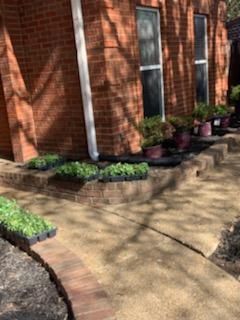 Brick house with sidewalk; landscaping with plants and flower pots.