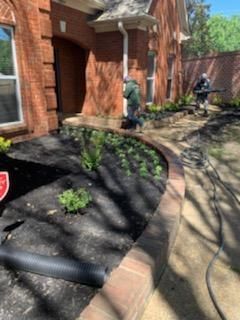 Workers using equipment to landscape a house with a brick facade and a garden bed.