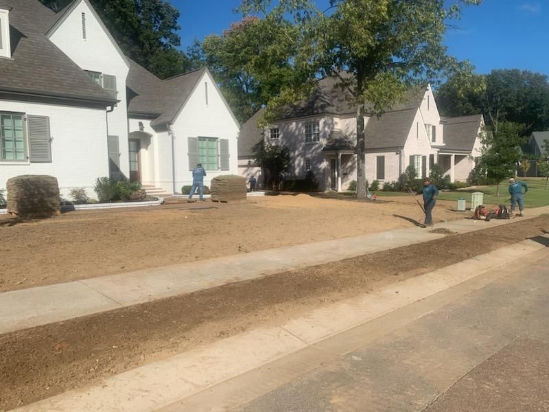 Workers preparing lawn in front of several white houses on a sunny day.