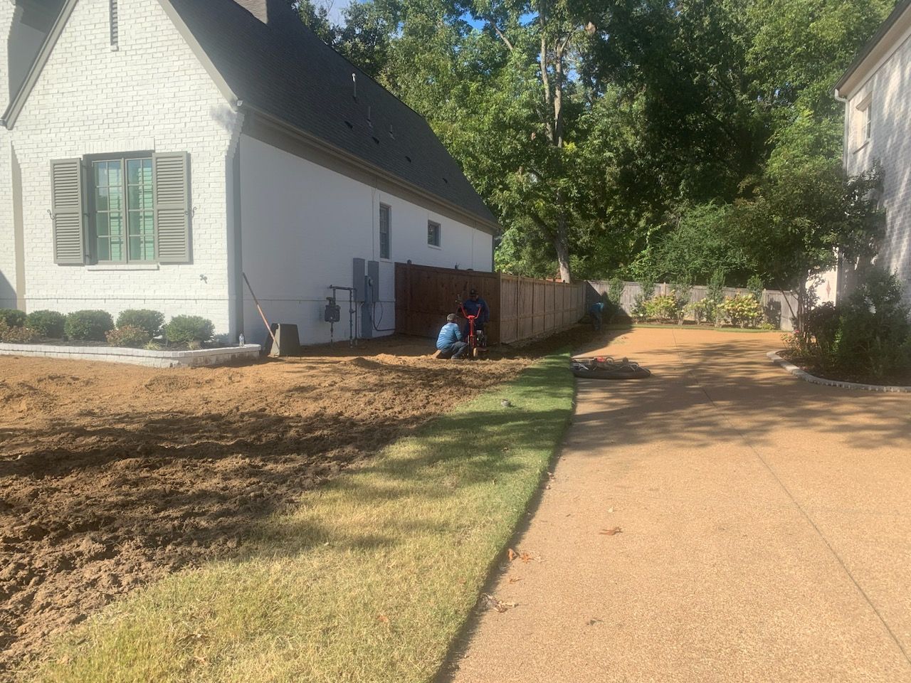A person working on landscaping next to a house. Dirt patch and grass in front.