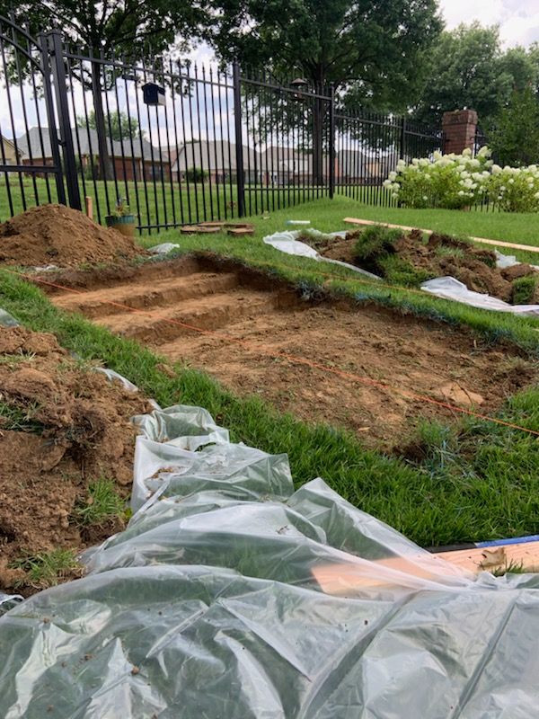 Backyard excavation for landscaping with soil, sod, fencing, and plants.