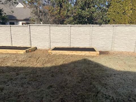 Two wooden raised garden beds in a backyard with a gray fence and dormant grass.