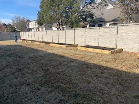 A backyard with rectangular garden beds along a beige fence, person in the distance.