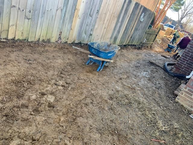 Blue wheelbarrow on muddy ground next to a wooden fence and brick wall.