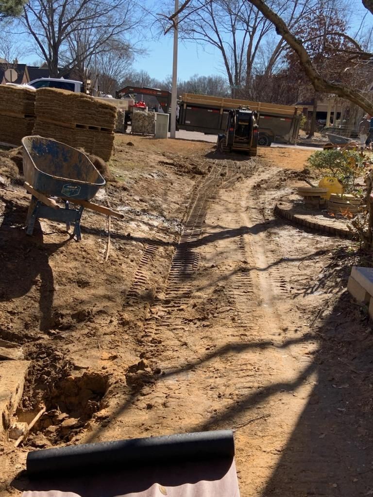 Construction site with dirt path, wheelbarrow, and small loader. Bright, sunny day.