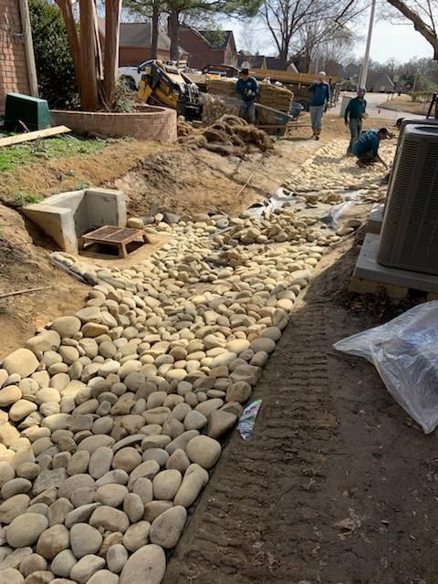 Workers installing a rock-lined drainage system along a residential property.