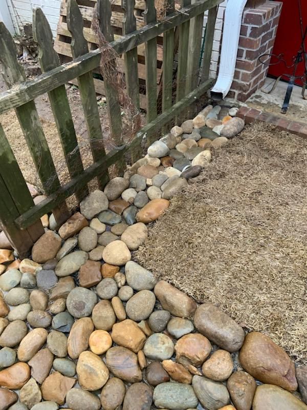 Rocks and mulch border a wooden fence and brick wall.