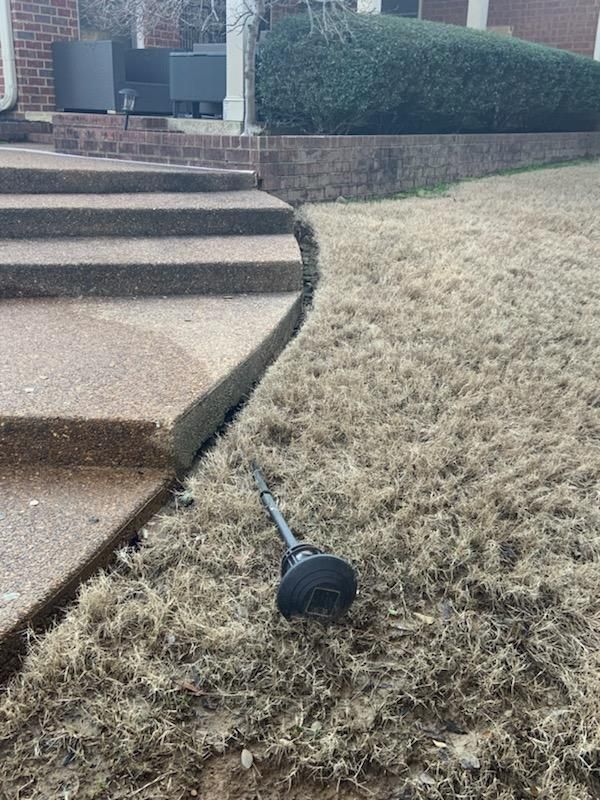 Concrete steps leading up to a house with a broken landscape light on a patch of dead grass.
