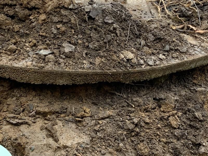 Cross-section of soil layers, showing dark topsoil over a layer of dark material, then lighter soil below.