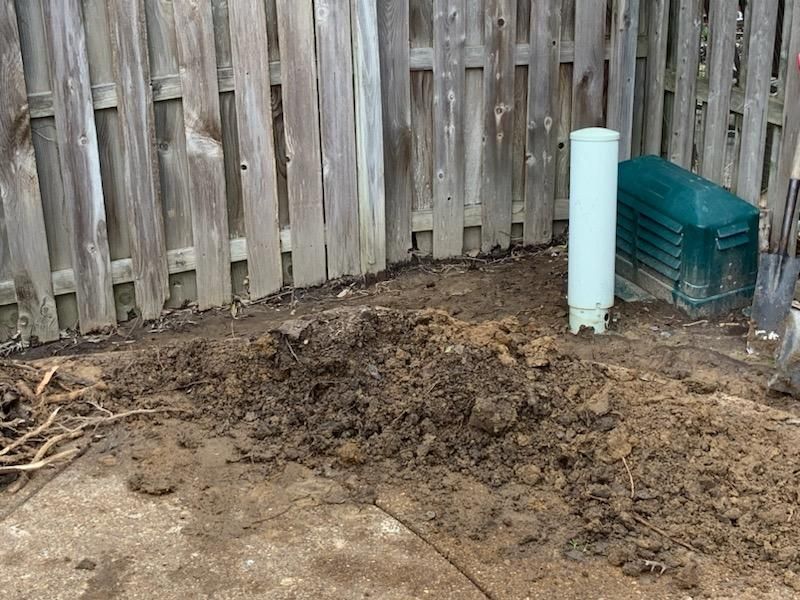 Pile of dirt next to a wooden fence, a white pipe, and a green box.