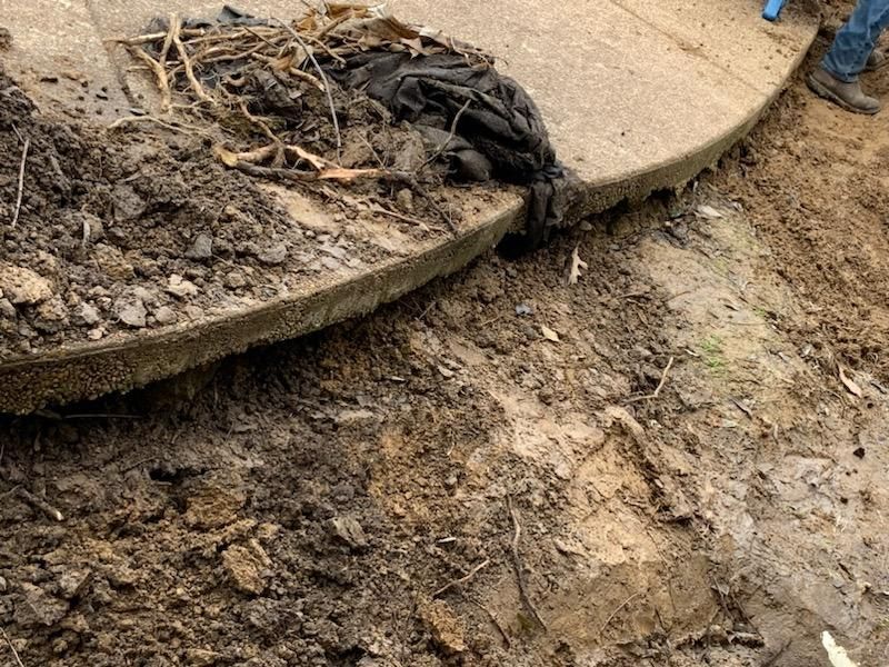 A damaged concrete curb with mud and debris, revealing a gap in the structure.