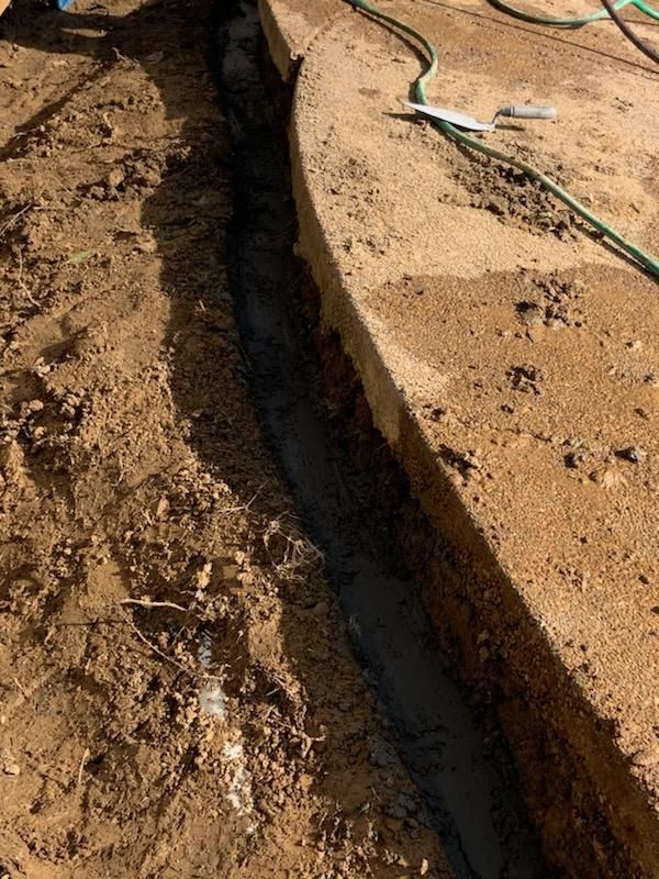Trench alongside a concrete curb, filled with mud. Dirt and hose nearby.