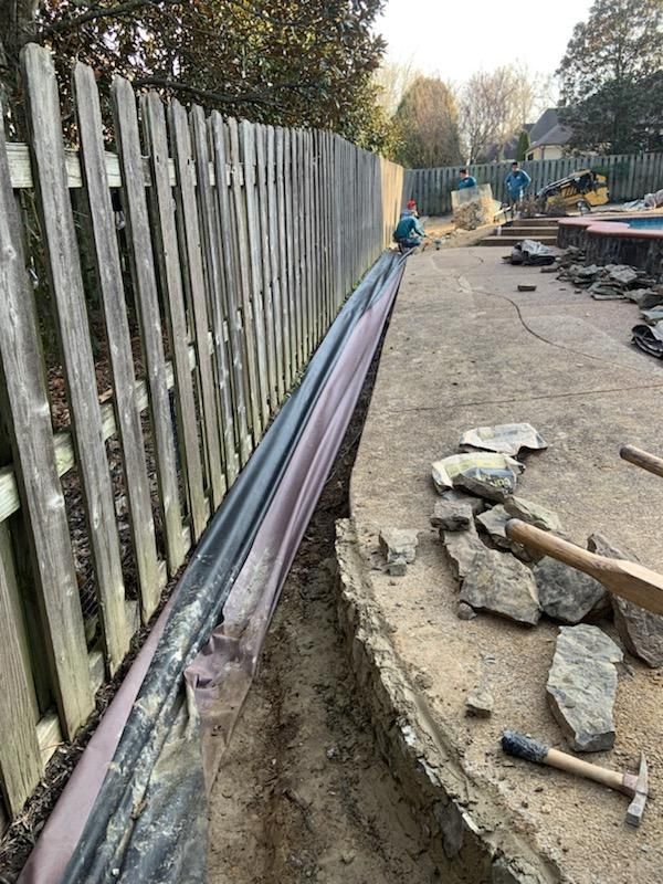 Trench next to a wooden fence containing pipes, construction in progress near a pool.