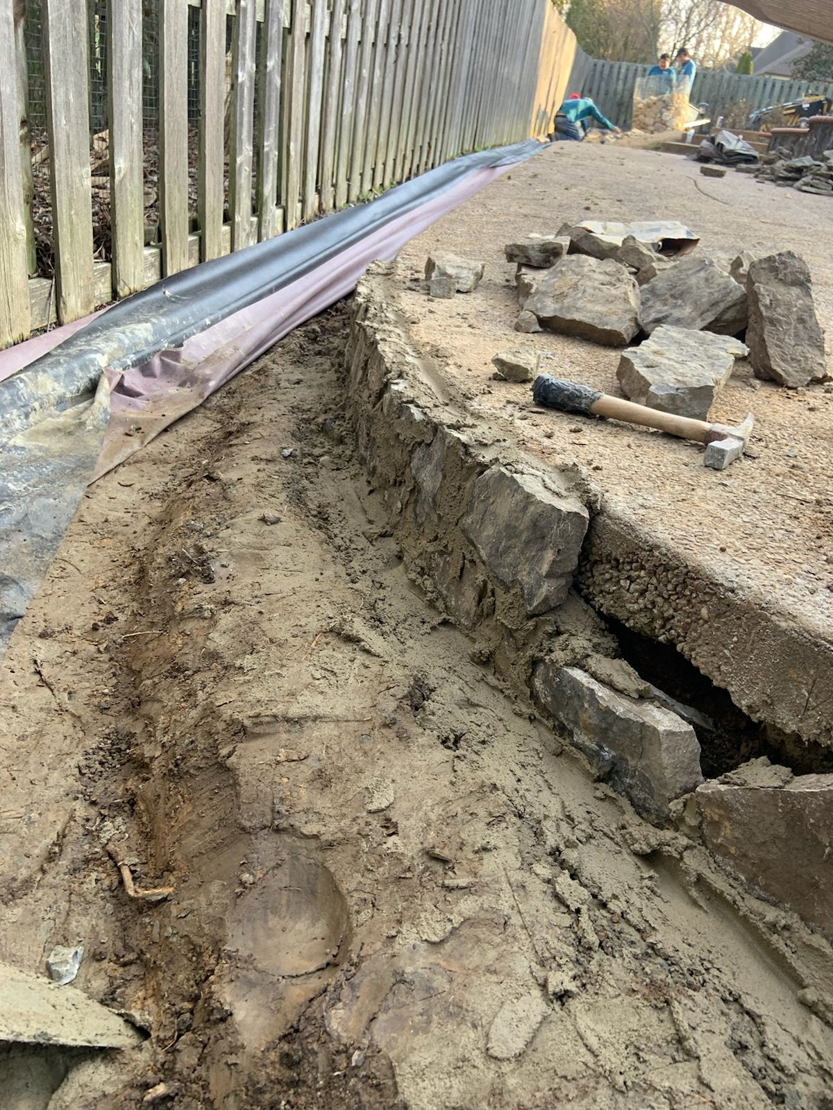 Construction site. Trench next to a fence, broken concrete, hammer, and dirt.