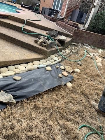 A garden bed under construction, with rocks, black fabric, hose, and steps leading to a pool.